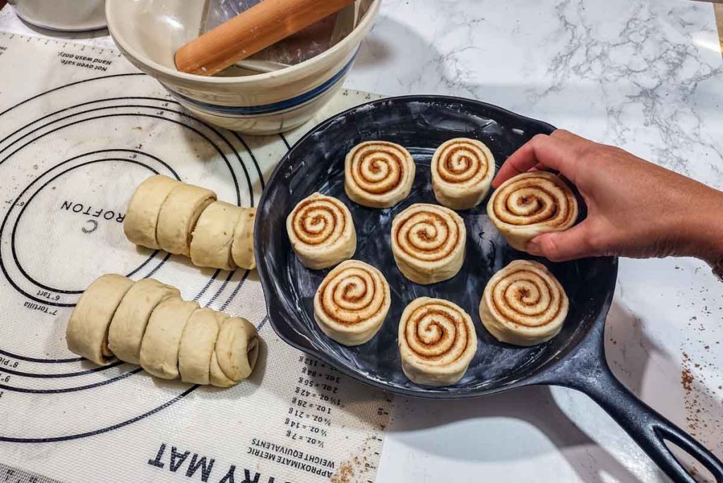 hand holding a piece of cinnamon roll in the cast iron pan