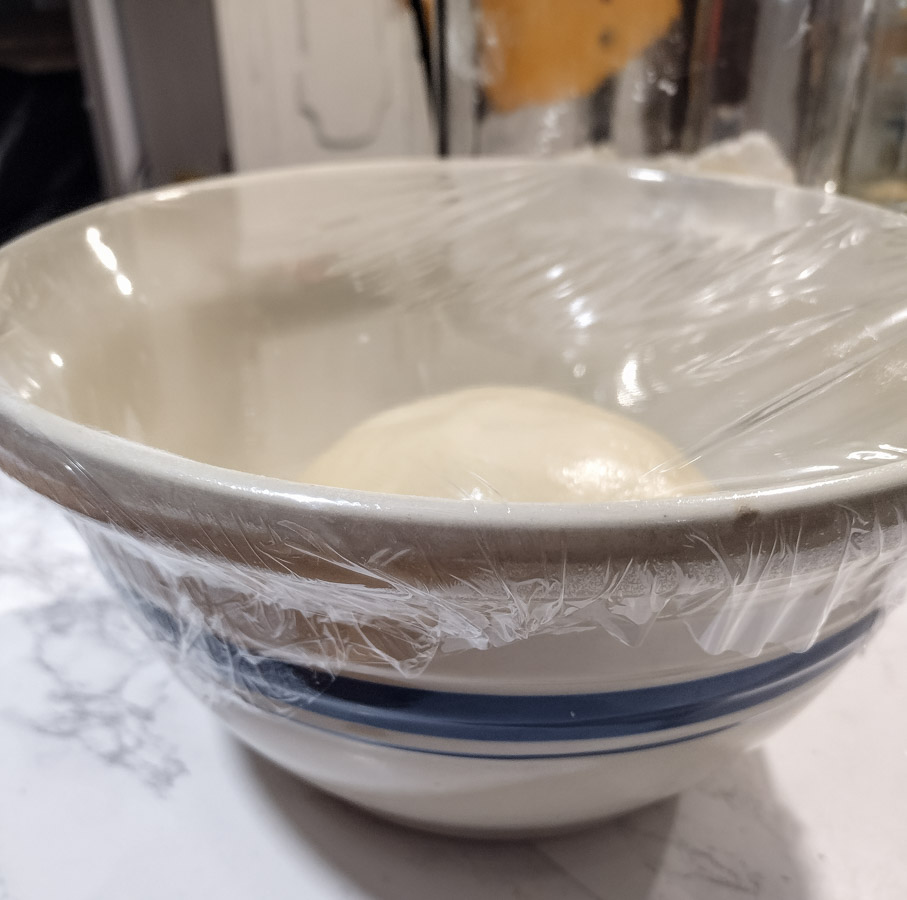 mixing bowl halfway filled with dough covered with plastic wrap