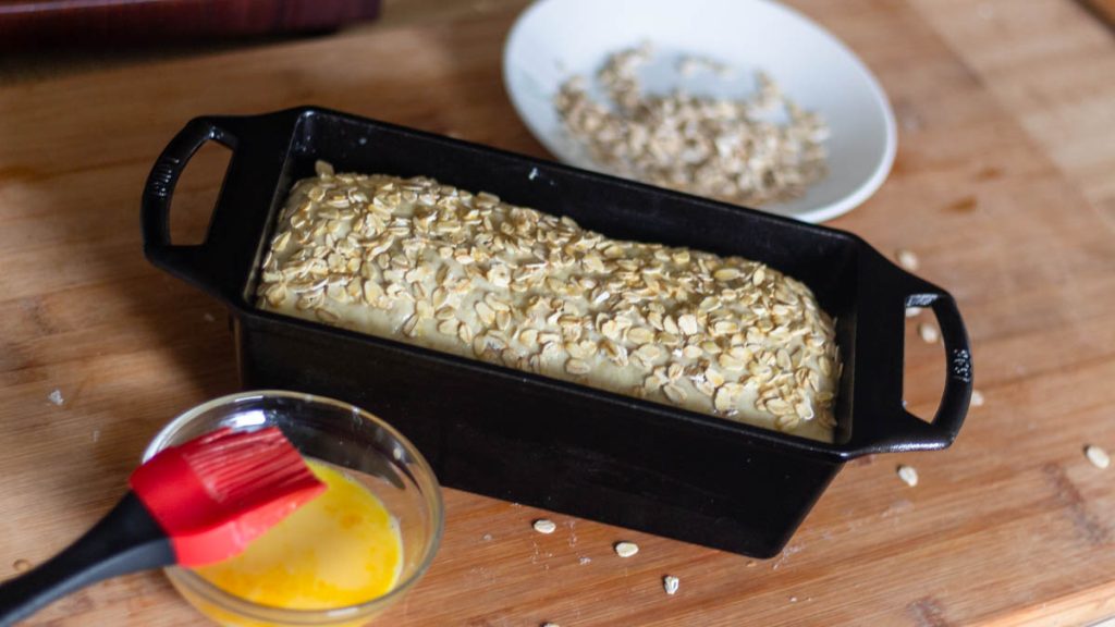 honey oats wet dough inside loaf cast iron pan on a wooden board