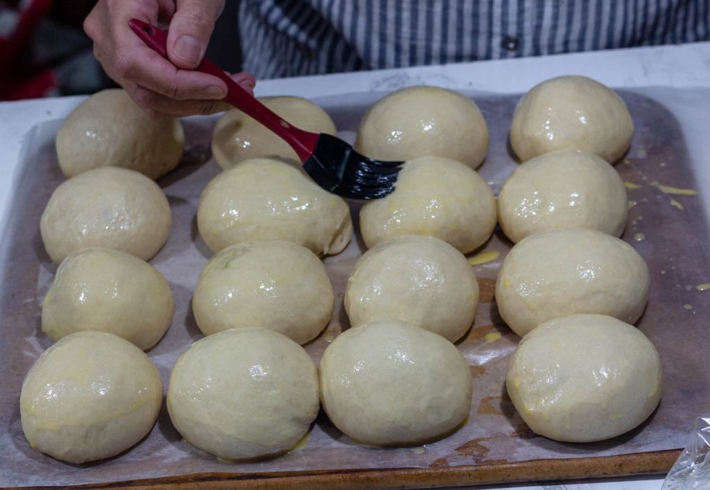 hand brushing liquid over sourdough brioche rolls