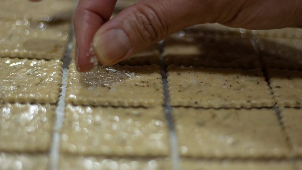 hand placing salt on wet sourdough crackers dough