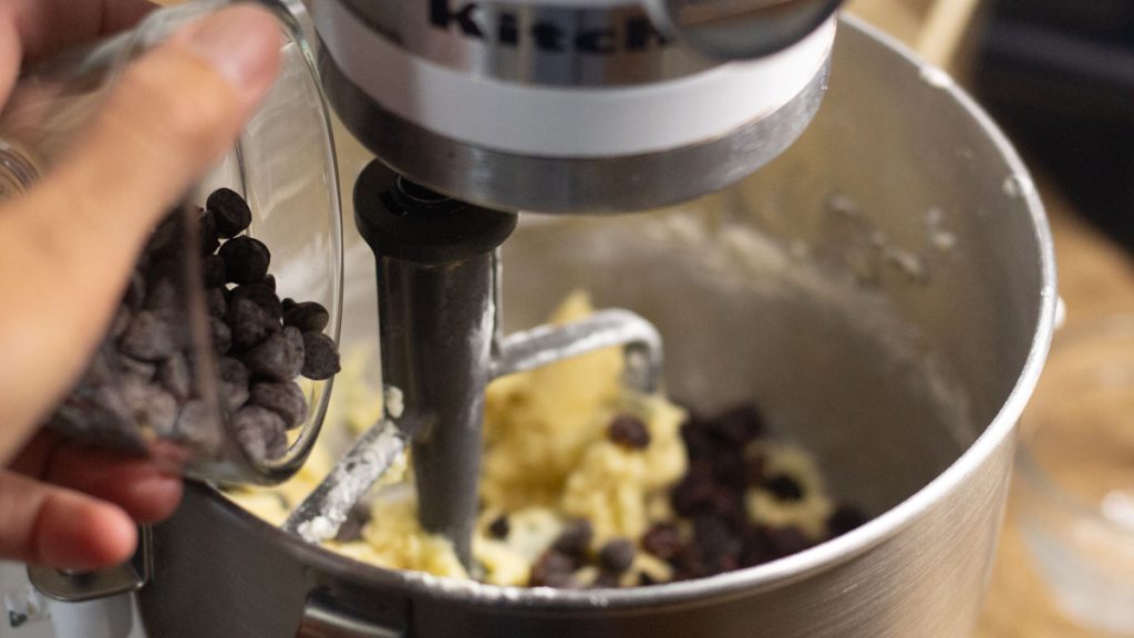 hand dropping chocolate chips inside the mixing bowl with wet ingredients of sourdough cookies