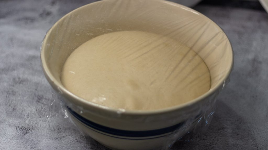 wet sourdough sandwich bread dough inside mixing bowl covered by plastic wrap