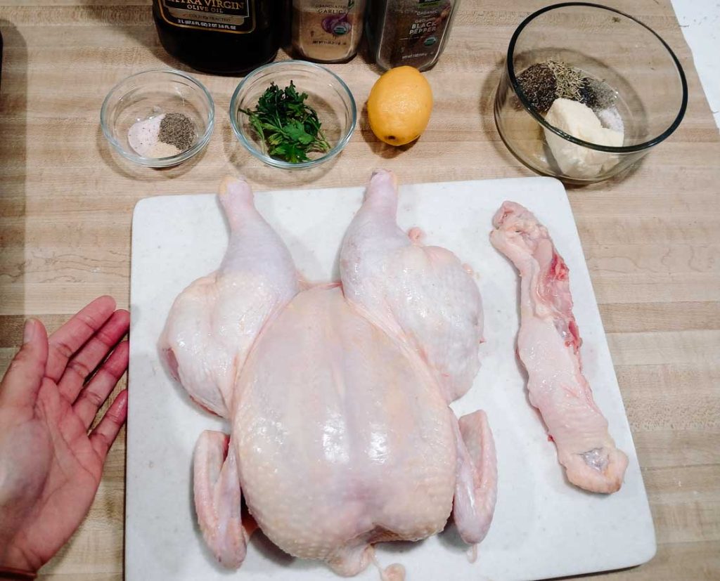 spatchcock chicken with ion chopping board surrounded with oil, spices and herbs