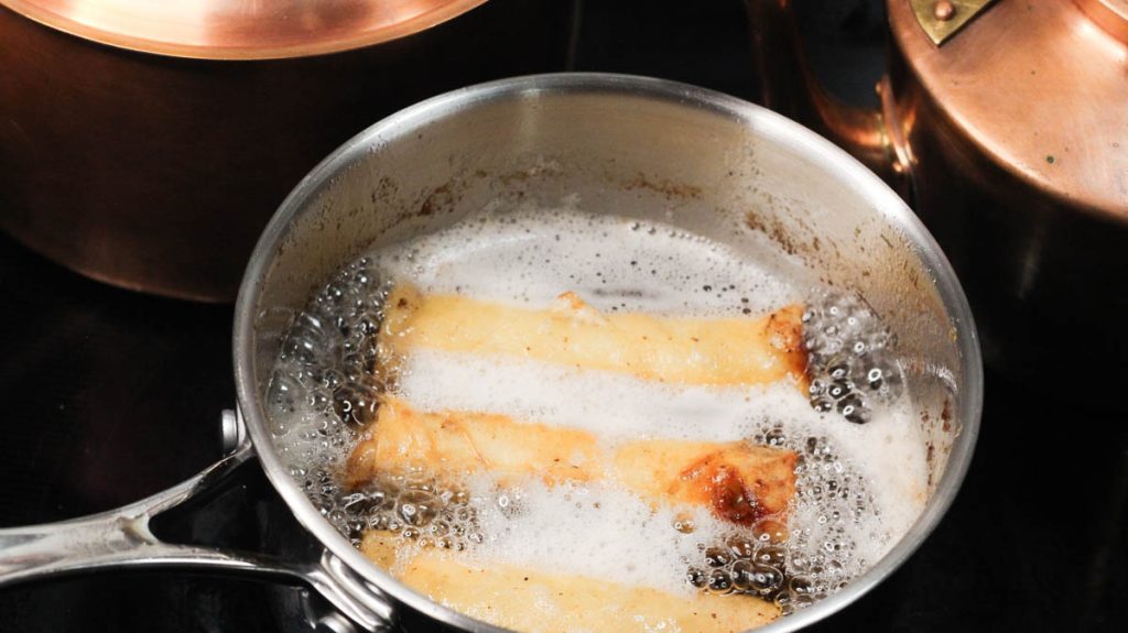 frying pan with bubbling oil and spring rolls