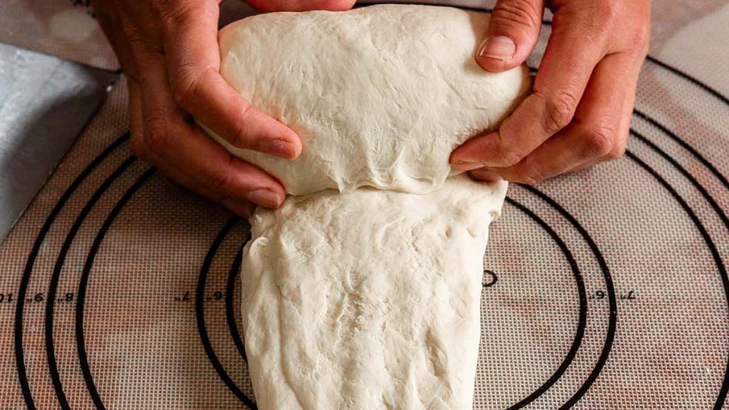 two hands rolling sourdough sandwich into a log shape