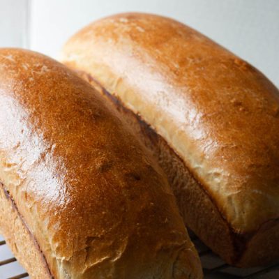 two loaves of baked sourdough sandwich bread on a cooling rack